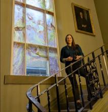 Dr Raewyn Martyn standing on a staircase in front of her artwork at the Grant Institute Cockburn Geological Museum stairwell site photographed in pale winter light. The calcium carbonate pigments from Portobello mussel shells refract light.