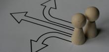Two small wooden game tokens with arrows pointing away from them in different directions