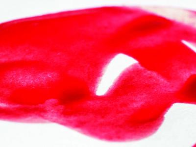 Red swirls of liquid emulating the flow of menses on a white fabric backdrop. Photo by Vulvani.