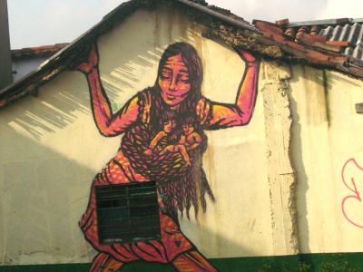 Street art from Colombia of a smiling woman holding up a roof, with babies held in a sling.