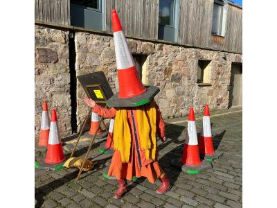 A woman with a traffic cone on her head, standing on a cobbled street.