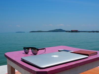 Thailand, Asia. Sunglasses, laptop and phone lie on a table in front of a beautiful seascape.