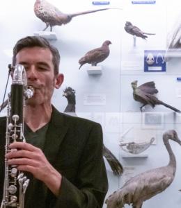 Dr Alex South Dr Alex South: a man playing a clarinet in front of a museum case filled with taxidermied birds