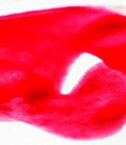 Red swirls of liquid emulating the flow of menses on a white fabric backdrop. Photo by Vulvani.