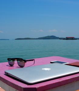 Thailand, Asia. Sunglasses, laptop and phone lie on a table in front of a beautiful seascape.